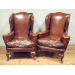 A pair of Georgian style brown leather studded wing backed easy chairs standing on cabriole legs