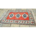 An Eastern rug, decorated three central lozenges on a red ground, within a multi border,