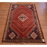 A Persian carpet with central medallion and geometric motifs on a red ground,
