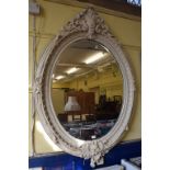 A white painted rococo style oval wall mirror, 104 cm wide,