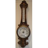 A late Victorian aneroid barometer, with thermometer, in a carved oak case,