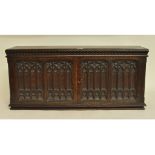 A Gothic carved oak collector's cabinet, the panel doors revealing a bank of drawers,