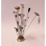 A silver and enamel hat pin, and others similar, on a silver pincushion,