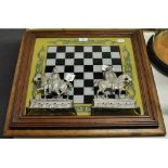 A glazed and framed painted chess board, 56 cm wide, and a pair of cast metal hearth ornaments,