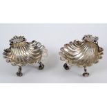 A pair of George II silver butter dishes, of shell form on three scroll feet, crested,