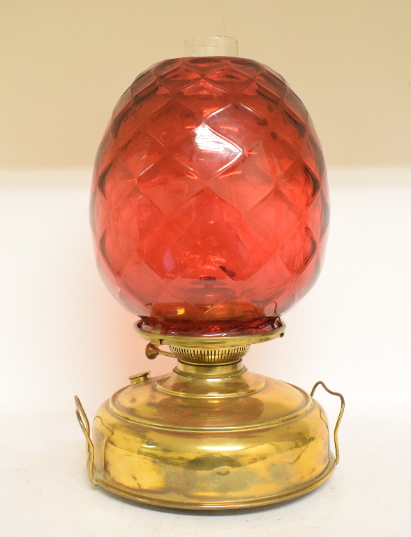 A large oil lamp, with a quilted cranberry glass shade on a brass reservoir,