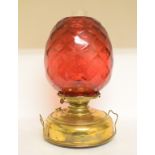 A large oil lamp, with a quilted cranberry glass shade on a brass reservoir,