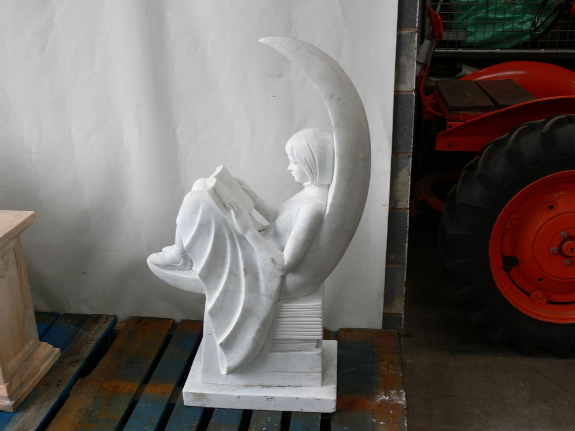 A marble sculpture of a young girl reading sat on a crescent moon. Please note this lot has a £10 +