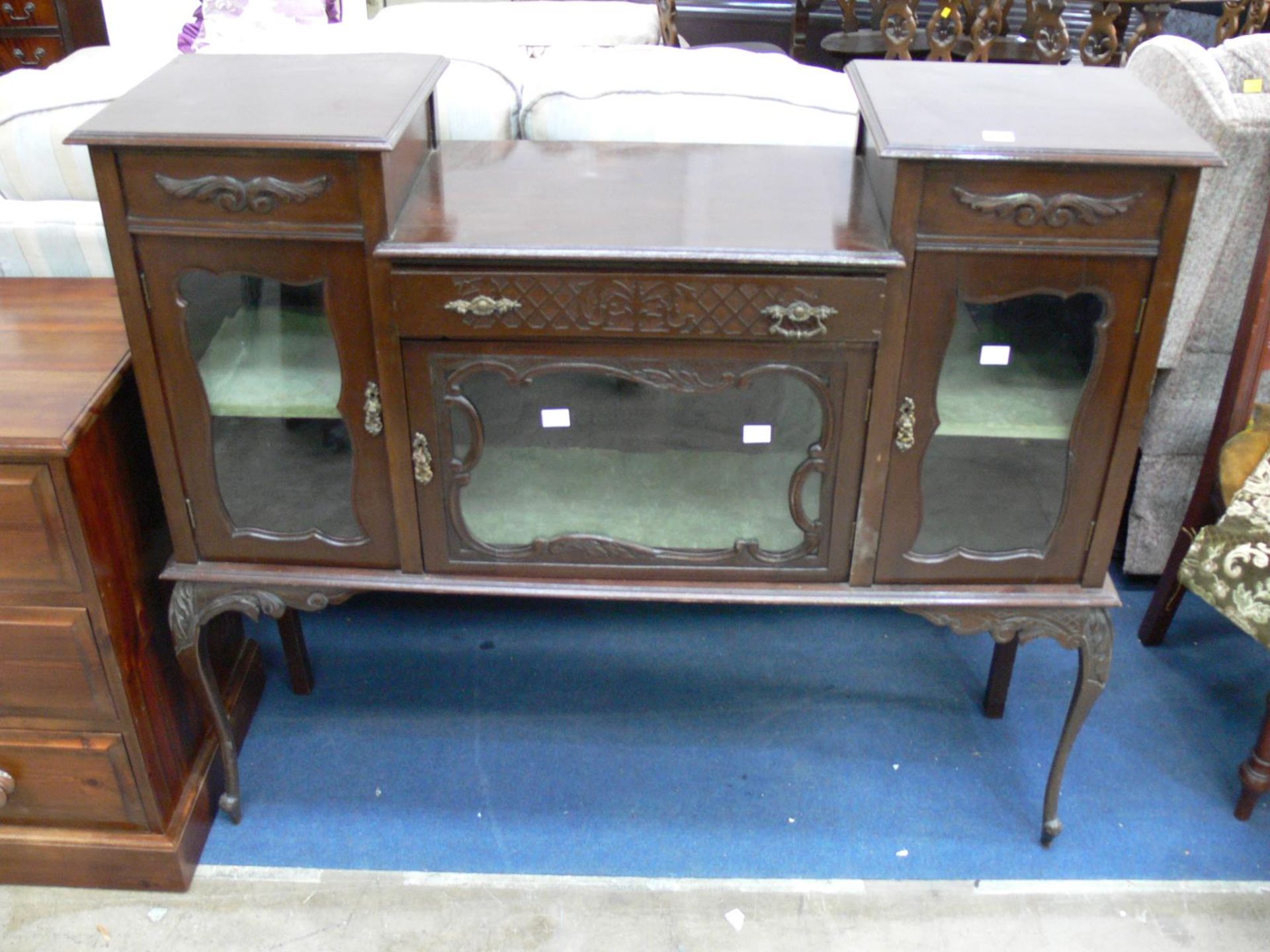 A display cabinet with lined shelves behind three glazed doors. A central drawer above the middle