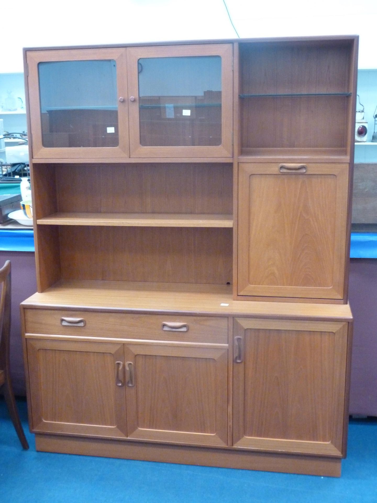 A teak wall unit with part glazed and shelved top, drinks cabinet to the sides and drawers and