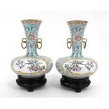 A pair of Chinese enamel vases on stands, decorated with flowers on a pale green ground, 20cm high.