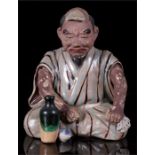 A 19th century Japanese pottery nodding figure in the form of a seated man holding a bottle of Saki,