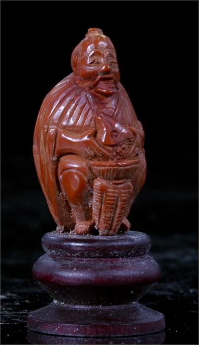 A Chinese carved heidao nut in the form of a seated man with a fish in a basket 4.5cm high