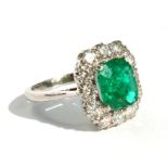 A platinum diamond and emerald ring set with a central square cut emerald, the emerald approximately