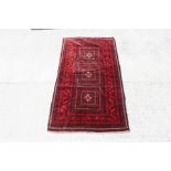 A Turkoman rug decorated with a repeat design within a stylised border, on red ground, 112cm by