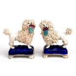A pair of Staffordshire figures in the form of poodles holding baskets of flowers with gilt anchor