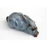 A well modelled glazed pottery figure in the form of a recumbent rabbit with glass eyes, 20cm (8ins)
