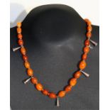 An amber necklace, twenty nine oval amber beads interspersed with white metal bell shaped drops,