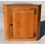 A 19th century stripped pine corner cupboard, the single door enclosing shaped shelves, 102cm (