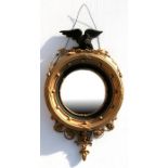 A gilt framed convex mirror, surmounted with a carved eagle, 43cm (17ins) wide.