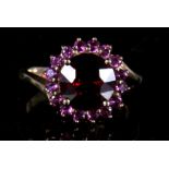 A 9ct cluster ring set with a large central deep red stone within a pink stone border. Approx UK