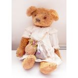 Gold plush bear wearing a vintage baby's dress with lavender bag and cap,