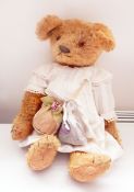 Gold plush bear wearing a vintage baby's dress with lavender bag and cap,