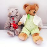 Grey bear wearing a knitted jumpsuit and a gold plush bear wearing a knitted jumpsuit with a cream