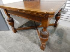 1930's oak extending dining table on stout carved cup and cover supports with X-stretchers