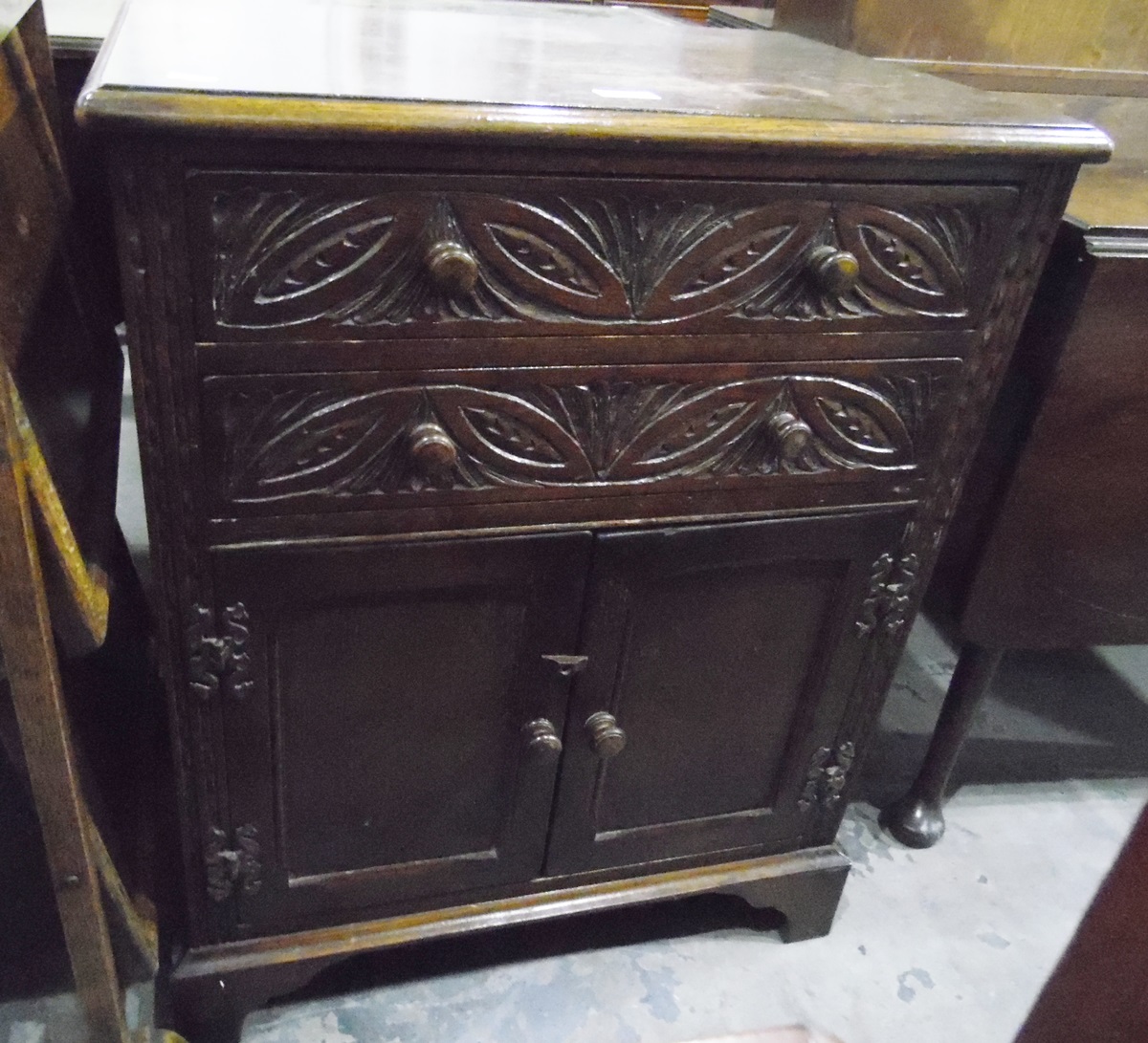 Carved oak cupboard with two long drawers, pair of panel doors below, raised on bracket feet,