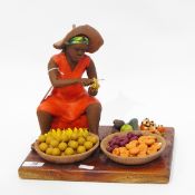 Pottery figure of a seated fruit seller, raised on a wooden plinth,
