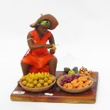 Pottery figure of a seated fruit seller, raised on a wooden plinth,