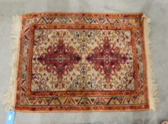 Eastern wool rug with two cherry red arabesques to the ivory field and having stylised leaf borders,