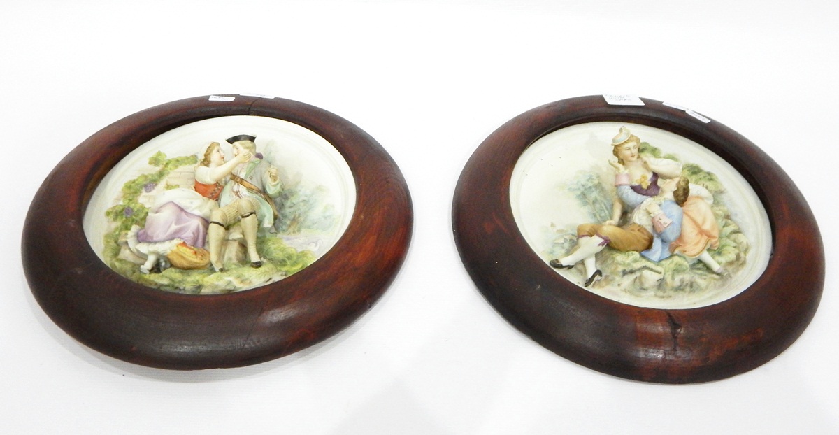 Pair of tinted bisque relief-moulded plaques of lovers, in wooden circular surrounds,