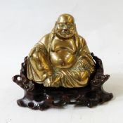 Brass model of a seated, laughing Buddha on carved hardwood throne, 23cm high