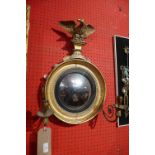 A Regency giltwood convex wall mirror with carved eagle surmount and twin sconces flanking the