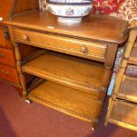 An Ercol style elm three tier drinks trolley fitted single drawer and raised on castors