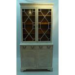 A white painted distressed bookcase having astragal glazed doors over two cupboard doors,