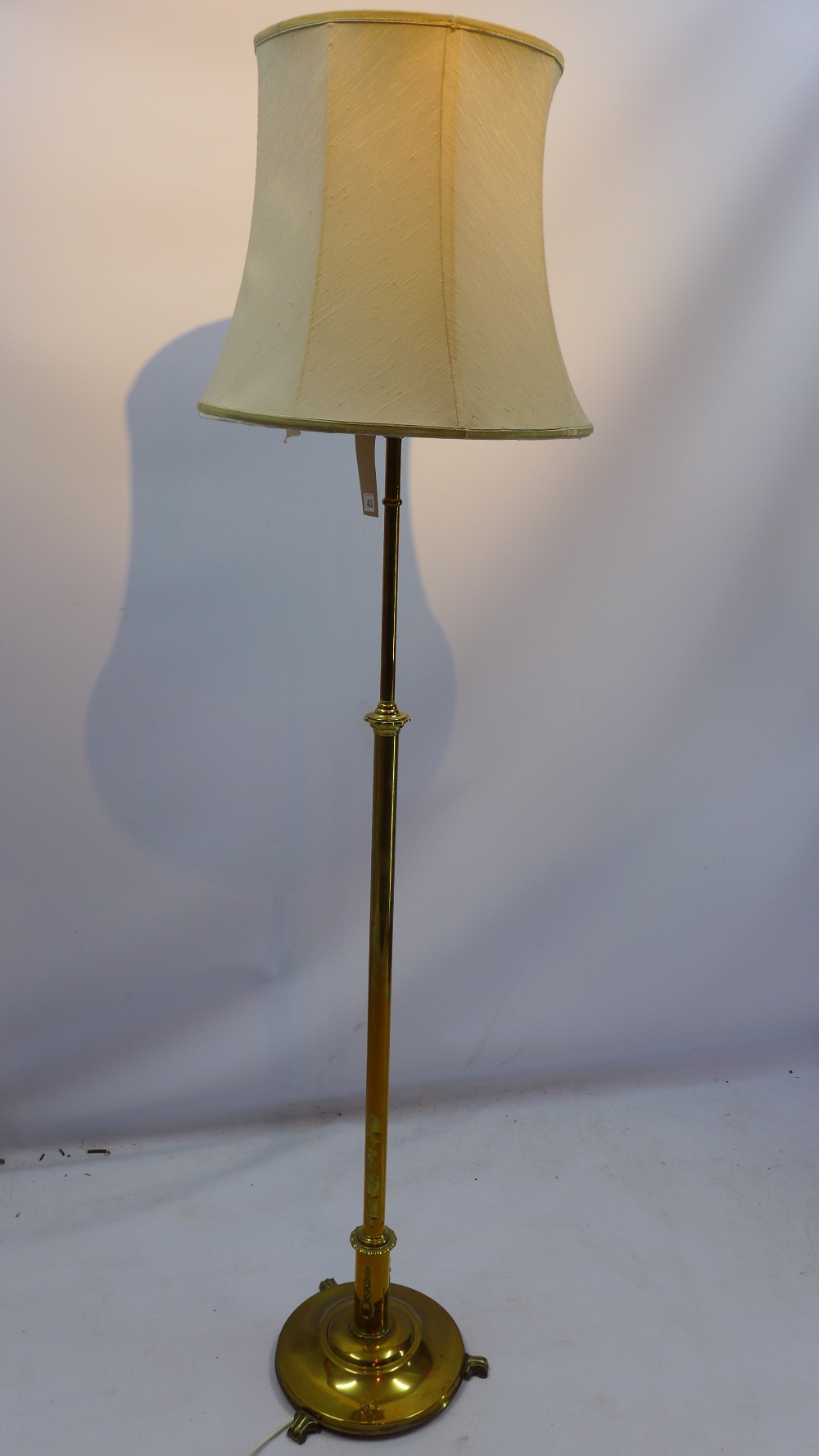 A brass standard lamp in the classical taste raised on circular base and three scroll feet H 145cm
