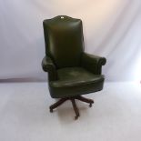 A 20th century green leather arm chair raised on mahogany swivel base and castors