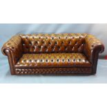 A tan leather three seater Chesterfield sofa having buttoned detail,