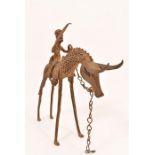 An African cast metal figure, brandishing a sword and seated on a mythical animal with horns and