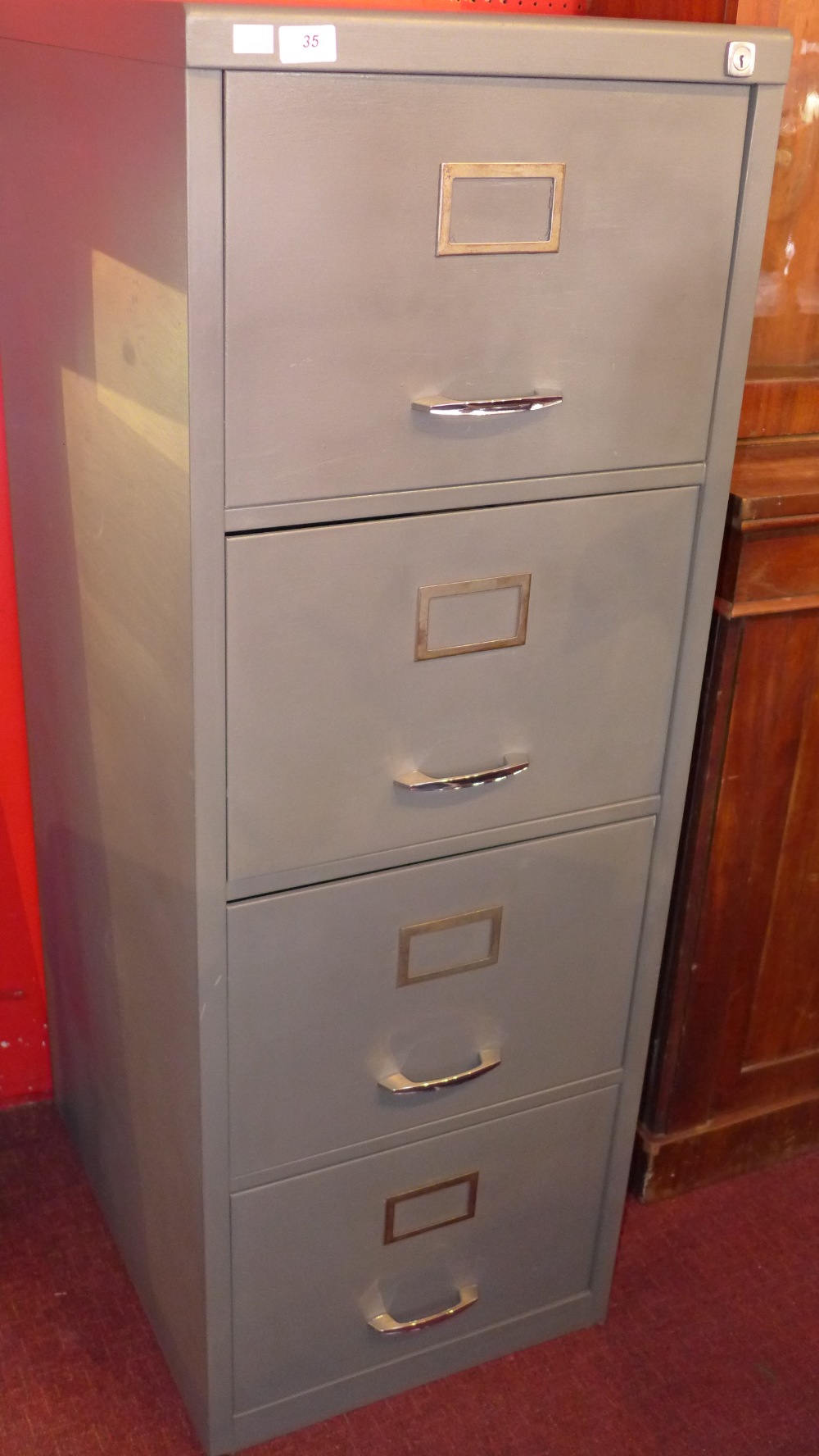 A metal four draw office filing cabinet 131cm in height.