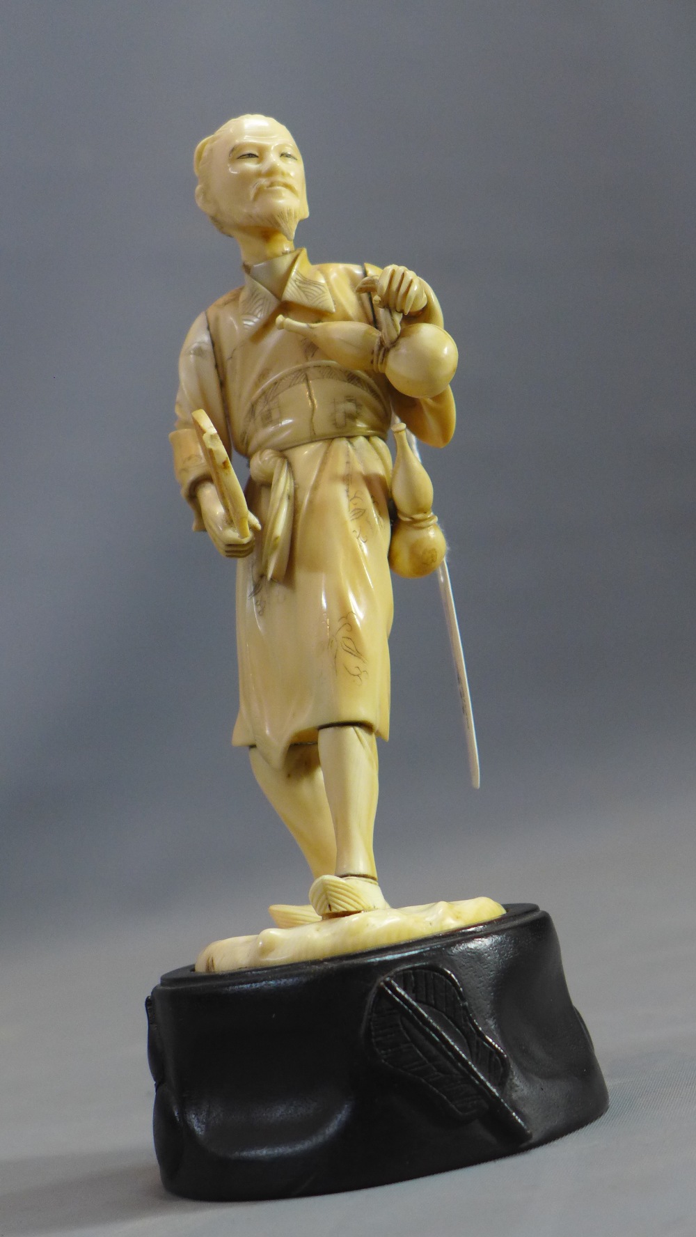 A 19th Century Japanese ivory carving of a man carrying two gourds and a fan.