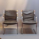 A pair of brown leather arm chairs, raised on brushed steel supports.