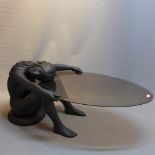 A contemporary coffee table in the form of a nude female holding an oval glass top.