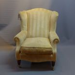 A contemporary wing back arm chair with stripped yellow fabric, raised on reeded legs and castors.