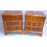 A pair of Georgian style yew wood serpentine fronted chests of three drawers raised on carved