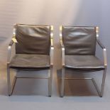 A pair of brown leather arm chairs, raised on brushed steel supports.