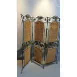 A green painted wrought iron dressing screen with wicker panels and holly leaf decoration.